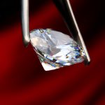 Diamant der von Pinzette gehalten wird vor rotem hintergrund